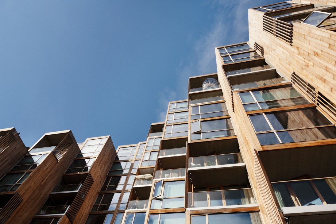 Upward view of 79&Park's wooden-clad facade with staggered balconies and windows against a clear blue sky.