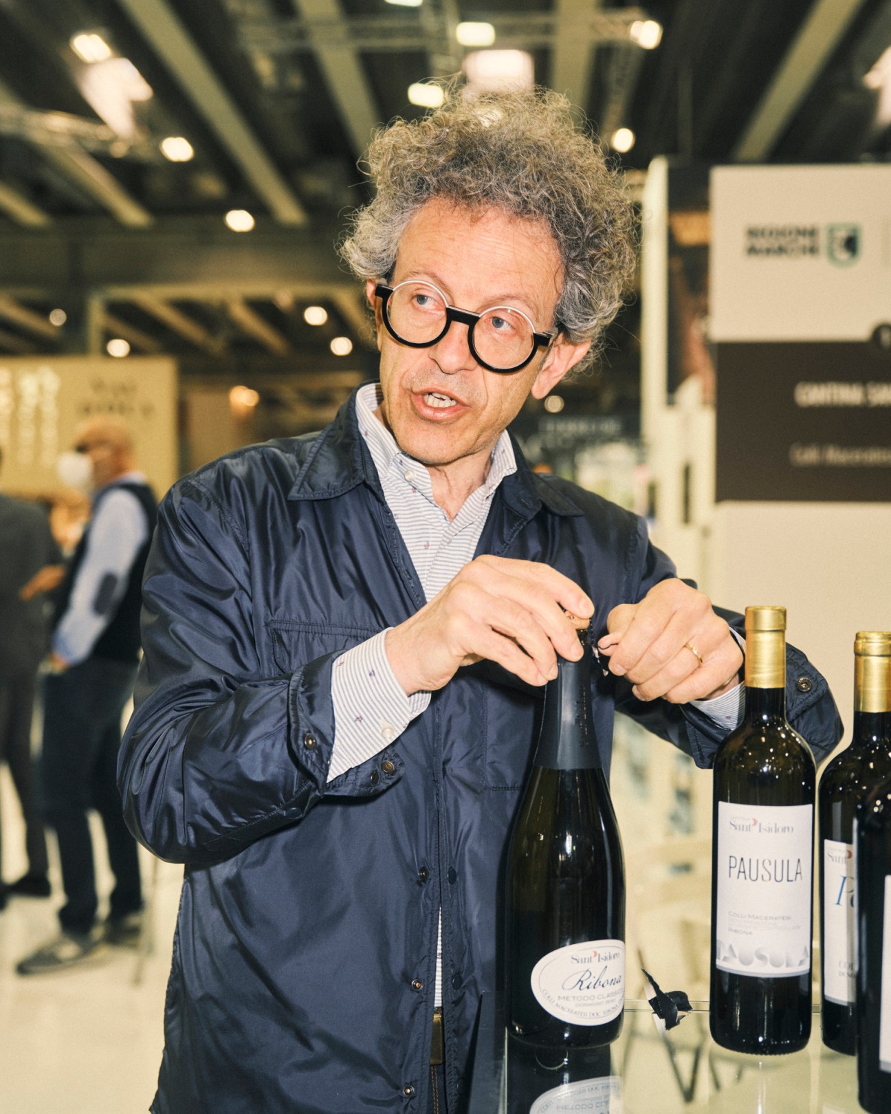 Man with curly hair and round glasses examining wine bottles at Vinitaly trade fair
