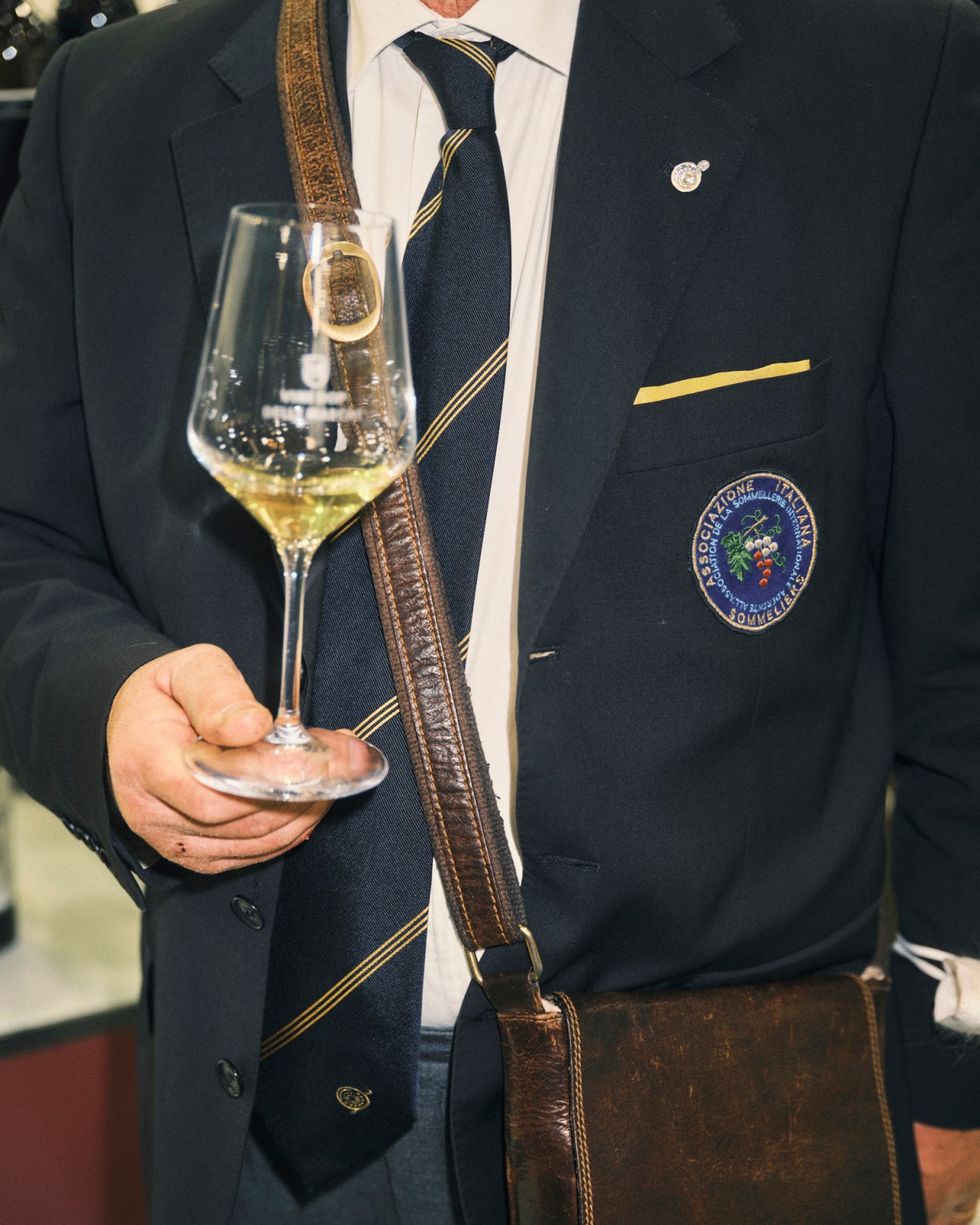 Well-dressed man in dark suit holding wine glass with sommelier badge at Vinitaly trade fair
