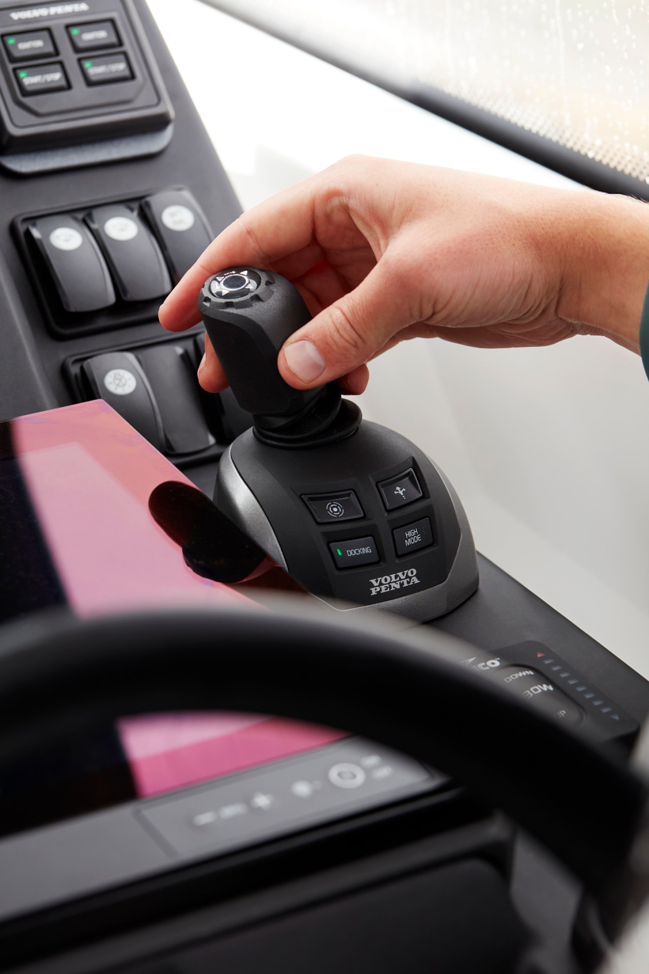 Hand operating a Volvo Penta joystick control system in a boat cockpit with various control buttons and switches