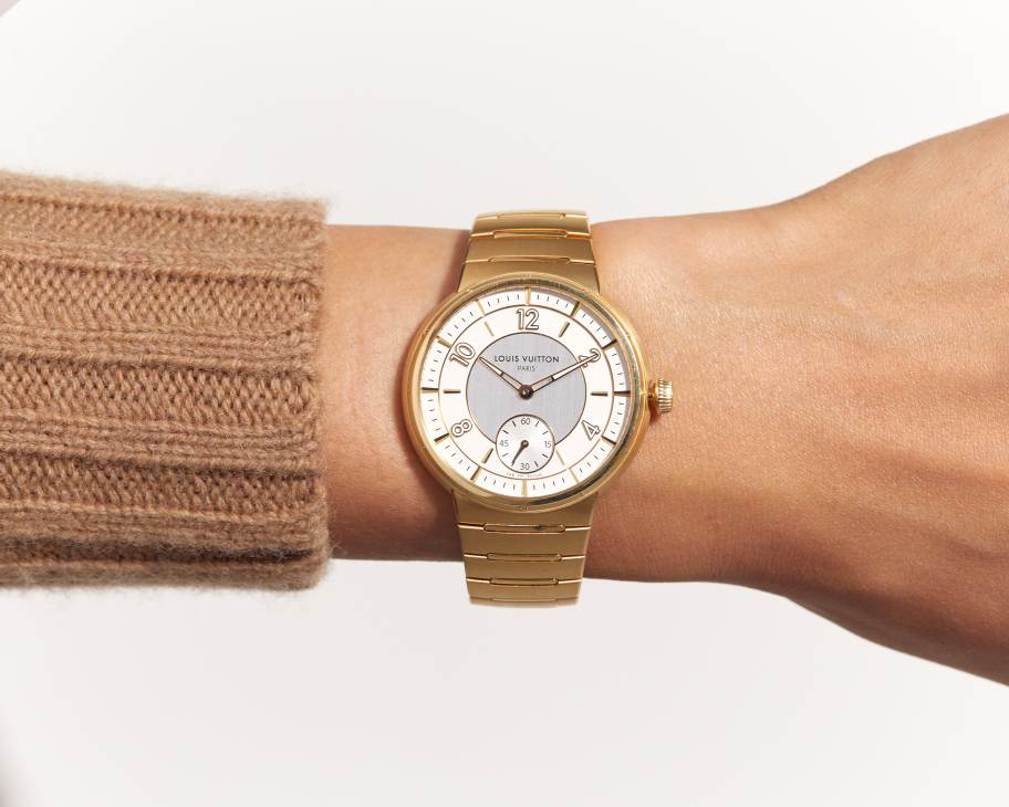 Louis Vuitton Tambour watch with gold case and white dial on beige sweater sleeve