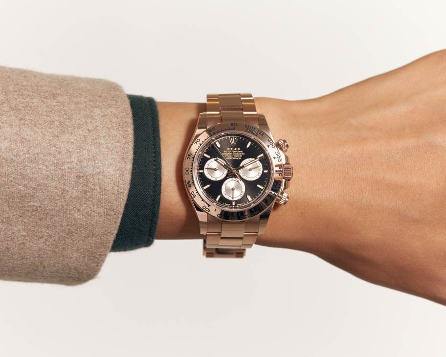 Rose gold Rolex Cosmograph Daytona watch with black dial and three white subdials on person's wrist