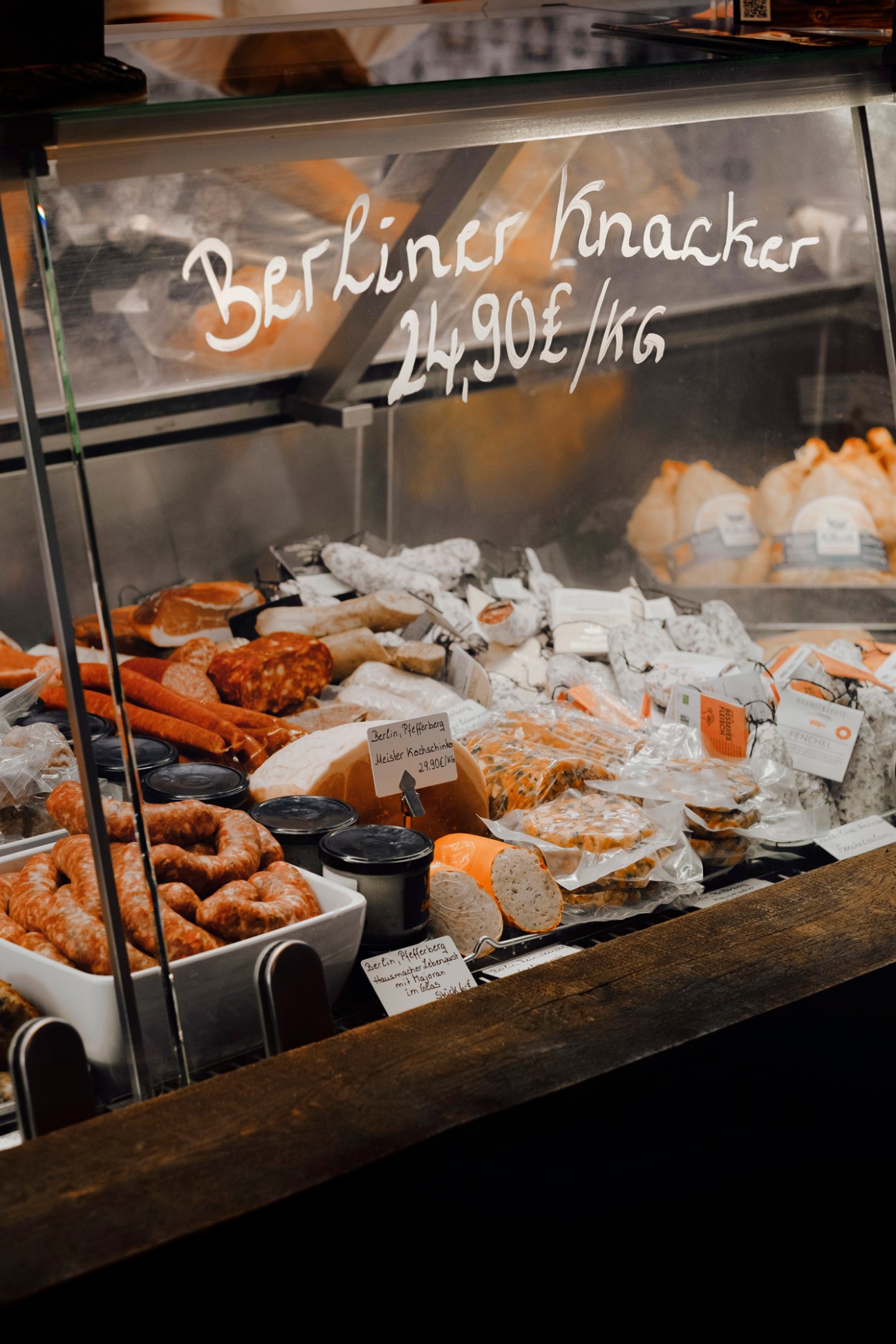 Glass display case showing various sausages, meats and prepared foods with handwritten price signs