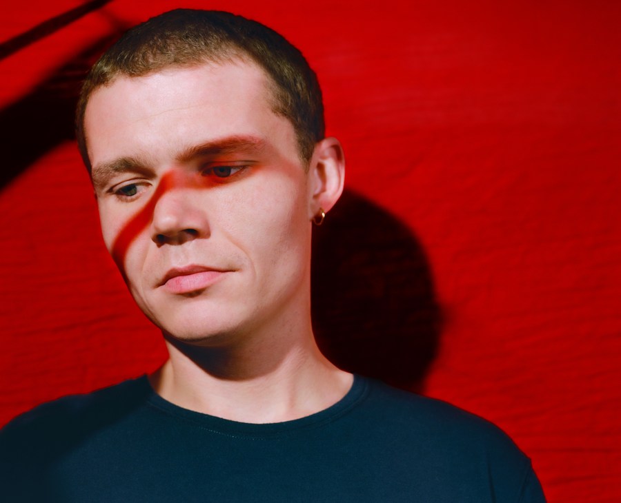 Portrait of Will Westerman against a red background, wearing a dark t-shirt.
