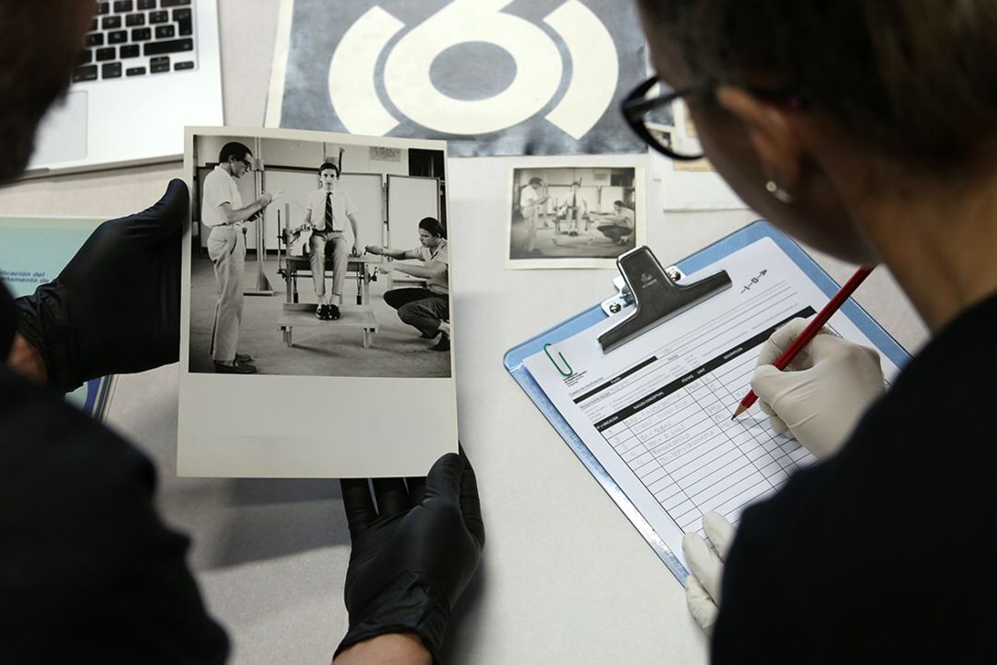 Person examining black and white photographs and documents at Fundación Ida design archive with clipboard