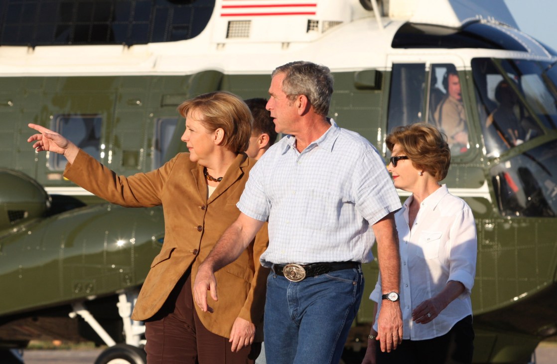 Angela Merkel and George W Bush walking together outdoors with helicopter in background
