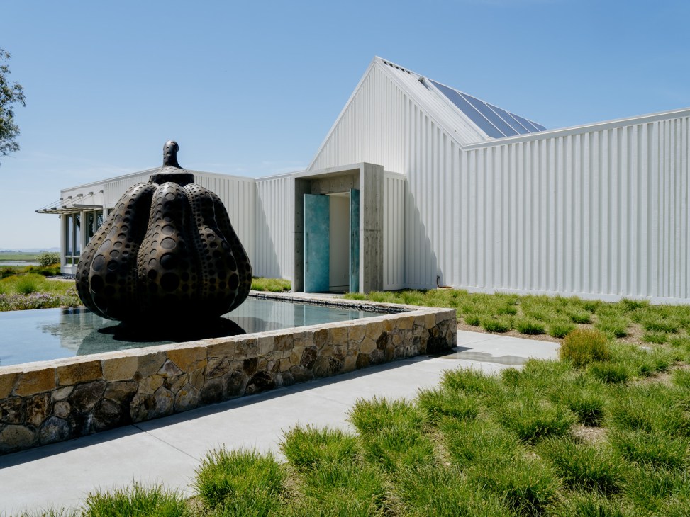 Black sculptural pumpkin installation by a reflecting pool near modern white metal architecture at Donum Estate.