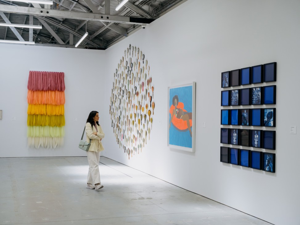 Woman viewing contemporary artworks displayed in a bright white gallery space with industrial ceiling.