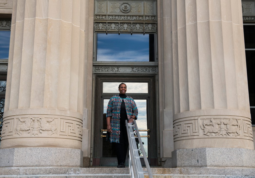 Person in colorful tweed coat standing in ornate building doorway with classical columns