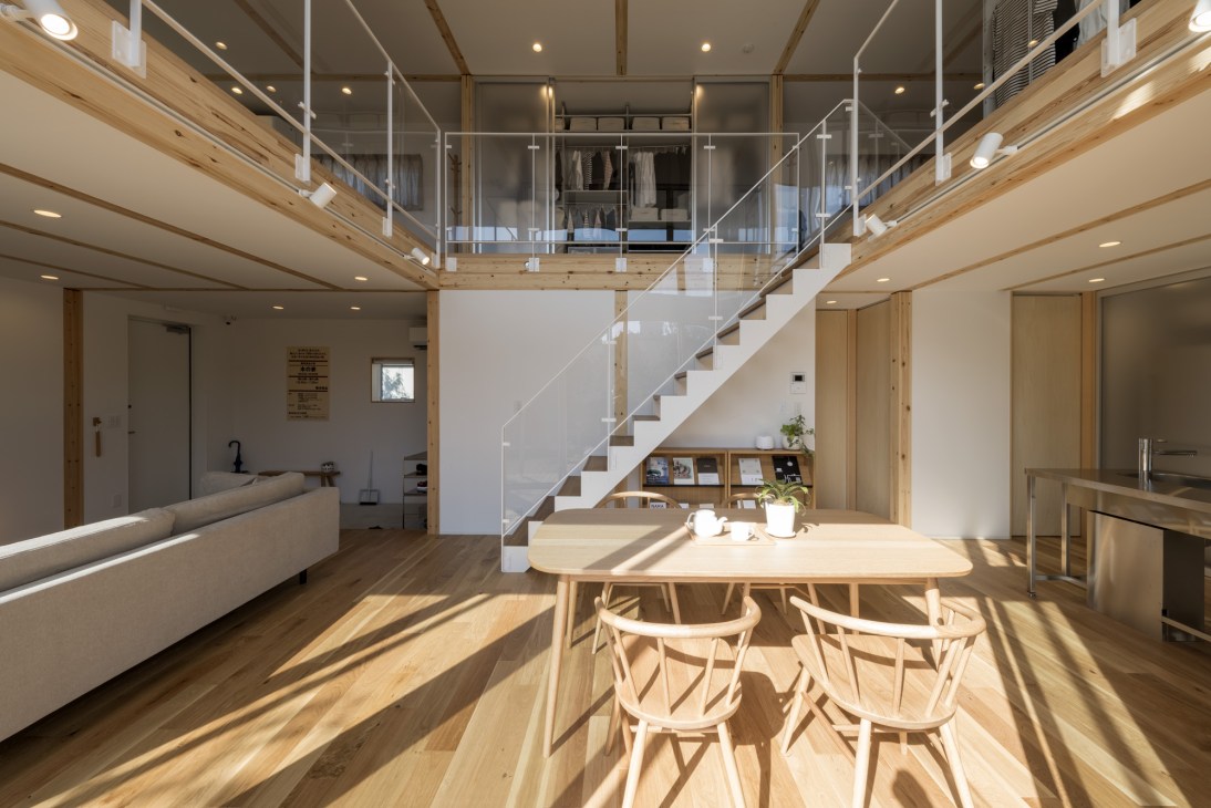 Minimalist wooden interior with dining table, chairs, mezzanine level, and storage under stairs in a Muji House.