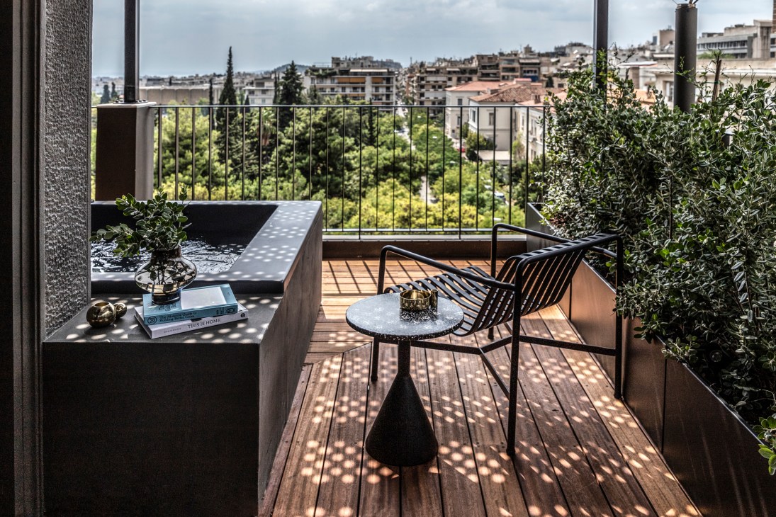 Modern terrace with wooden decking, black metal chair, small round table, and planters overlooking city buildings
