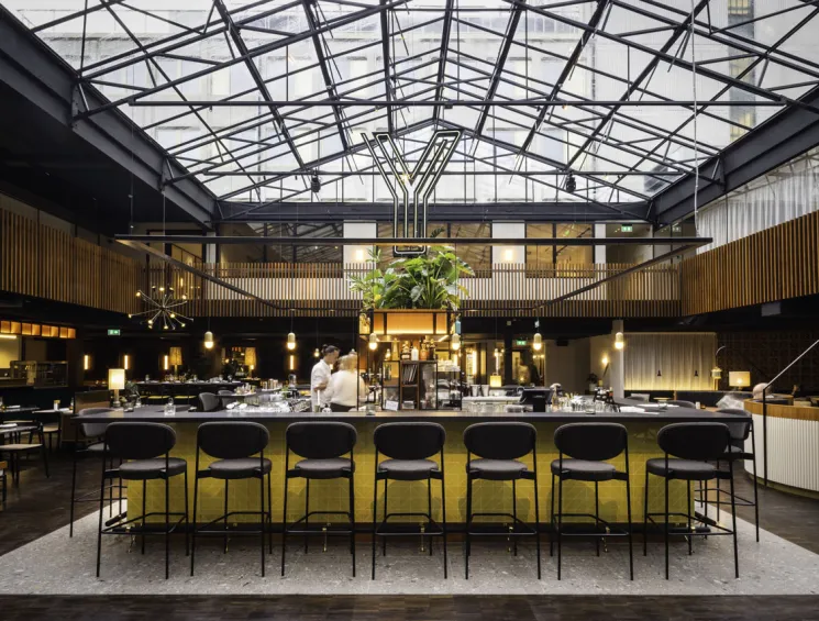 Glass-roofed restaurant at Yalo Urban Boutique Hotel with central bar, black bar stools, wooden paneling, and hanging plants in Ghent