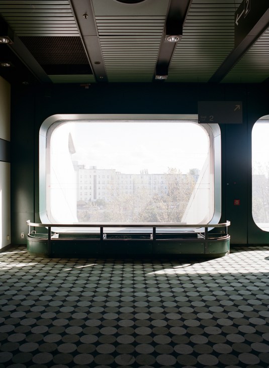 Large rounded window in International Congress Centre showing Berlin cityscape, with green wall paneling and patterned floor.