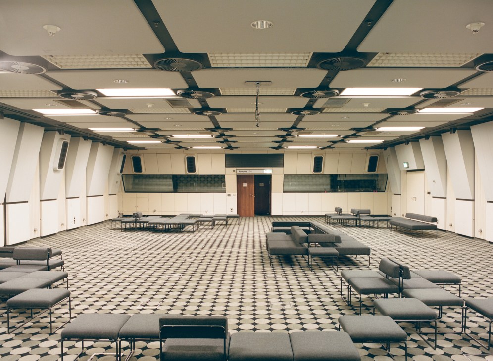 Windowless conference room with geometric patterned flooring, suspended ceiling with integrated lighting, and modular seating arrangements.