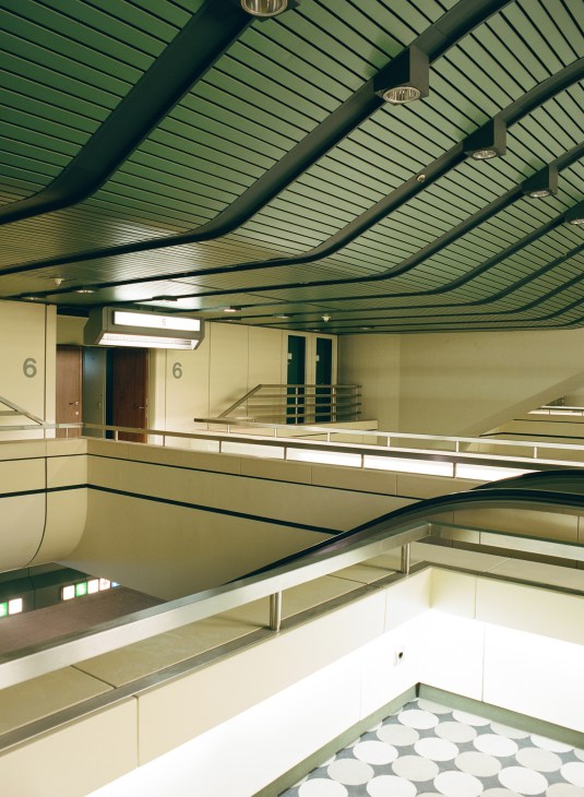 Multi-level interior hallway of the International Congress Centre with curved green ceiling, cream walls, and metal railings.