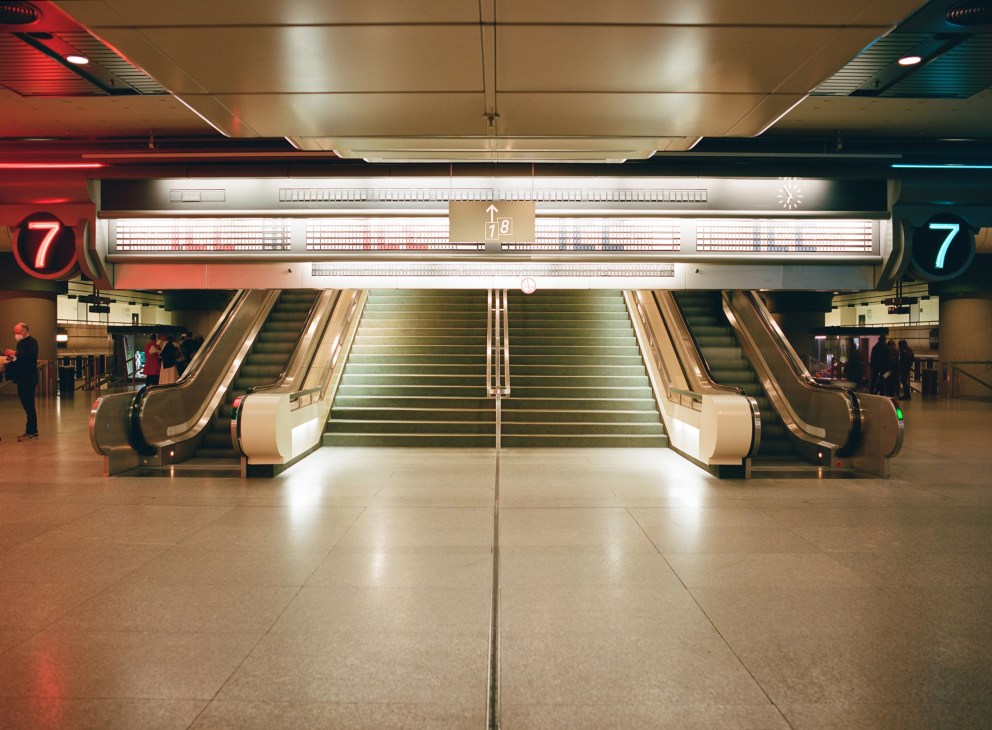 Modern staircase with escalators flanking a central flight of stairs in ICC Berlin's foyer, featuring neon signage and retro-futuristic design.