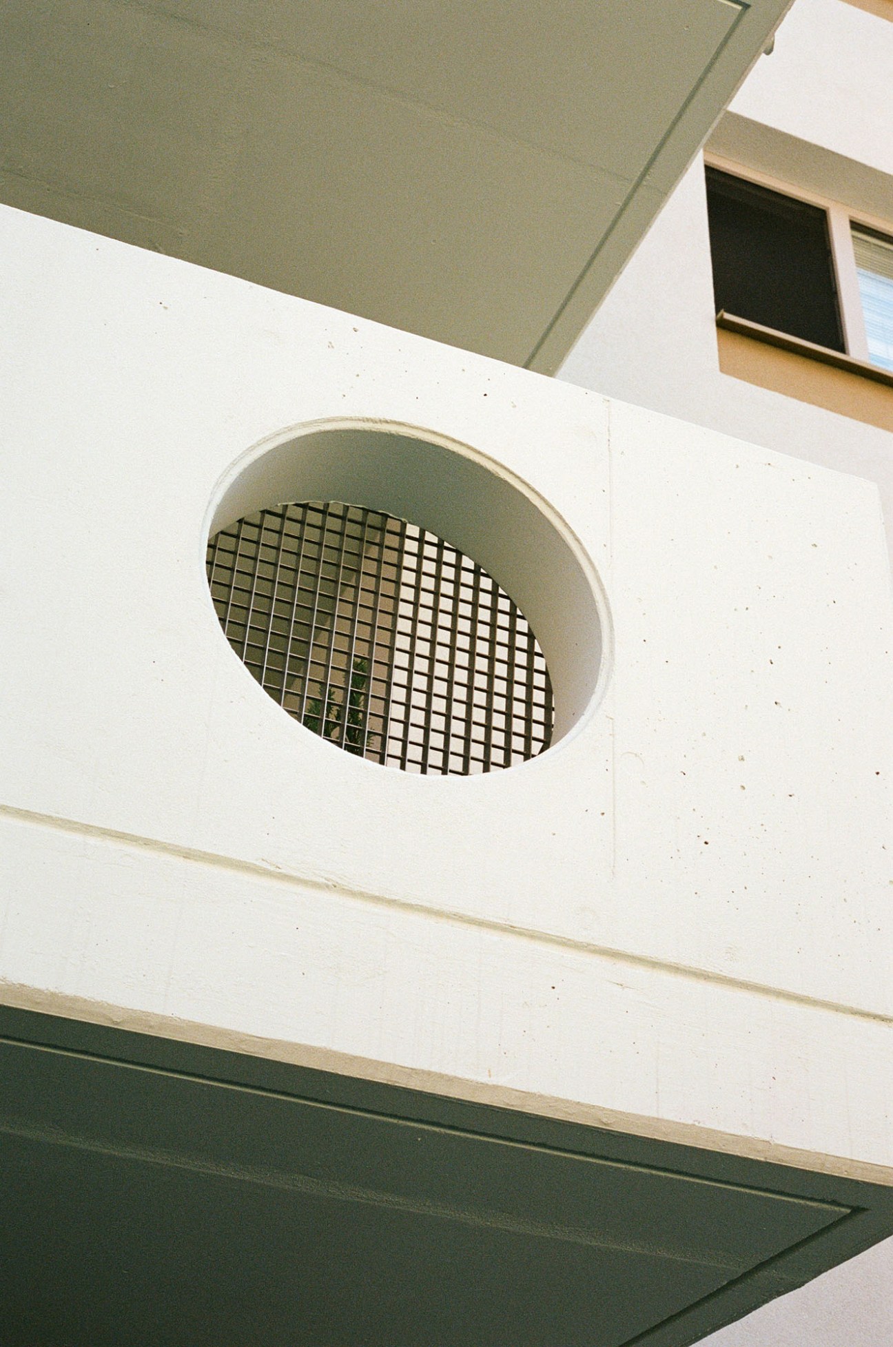Circular opening with grid pattern in white concrete wall showing architectural detail