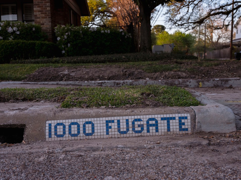 Blue and white mosaic tile street sign reading '1000 FUGITT' embedded in concrete curb