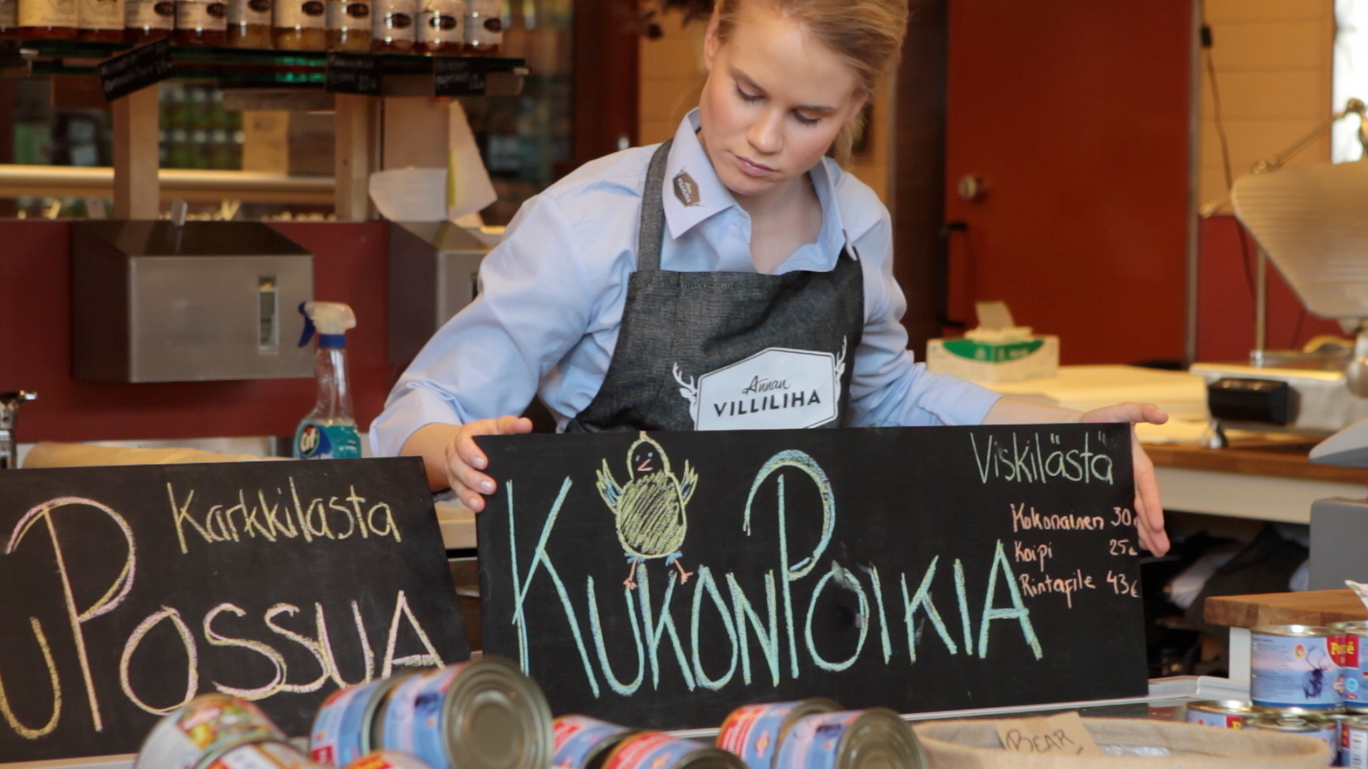 A woman arranging blackboard signs at a market.
