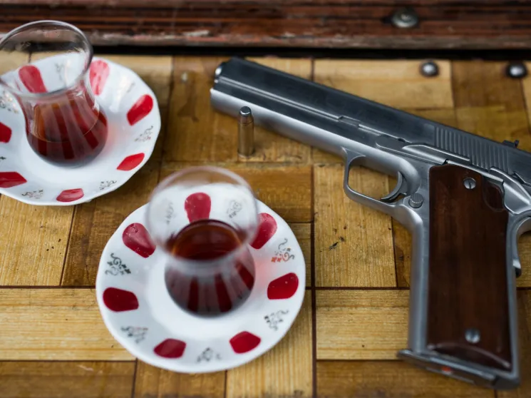 Gun lying on the table with cups of tea.