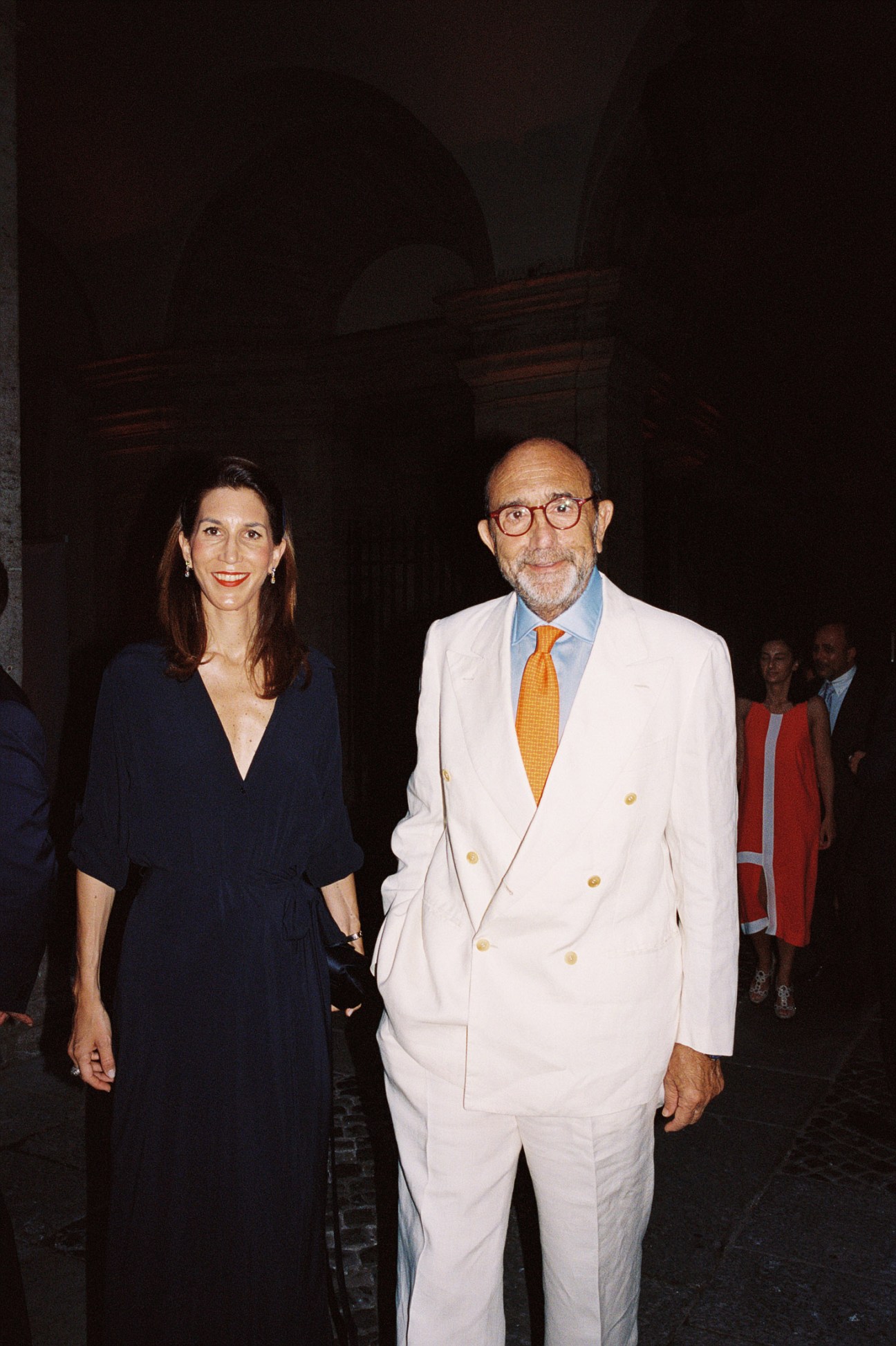 Man in white double-breasted blazer and orange tie and woman in dark dress at formal diplomatic reception