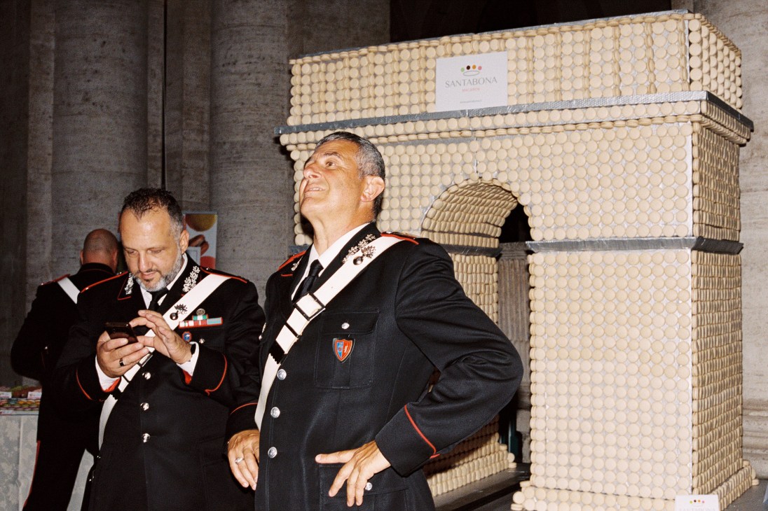 Two Italian carabinieri officers in formal dress uniforms looking upward at French embassy celebration