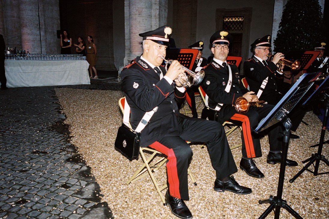 Italian Carabinieri military band members in formal uniforms playing brass instruments at a diplomatic event.
