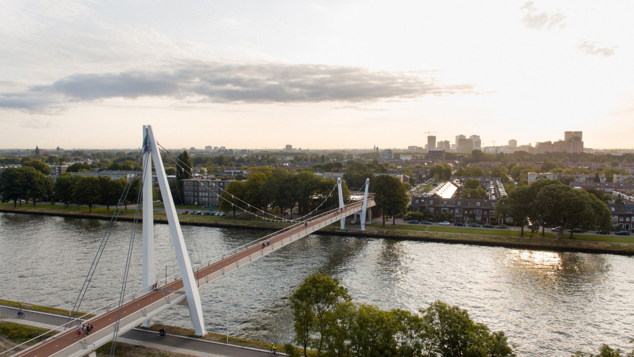 White cable-stay pedestrian bridge spanning a river with city skyline in background.