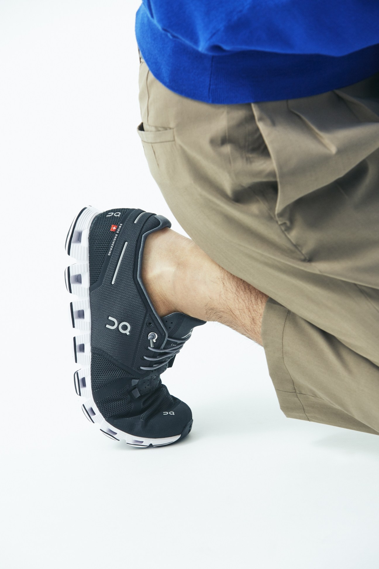 Model wearing a blue jacket, beige trousers, and On trainers with white soles.