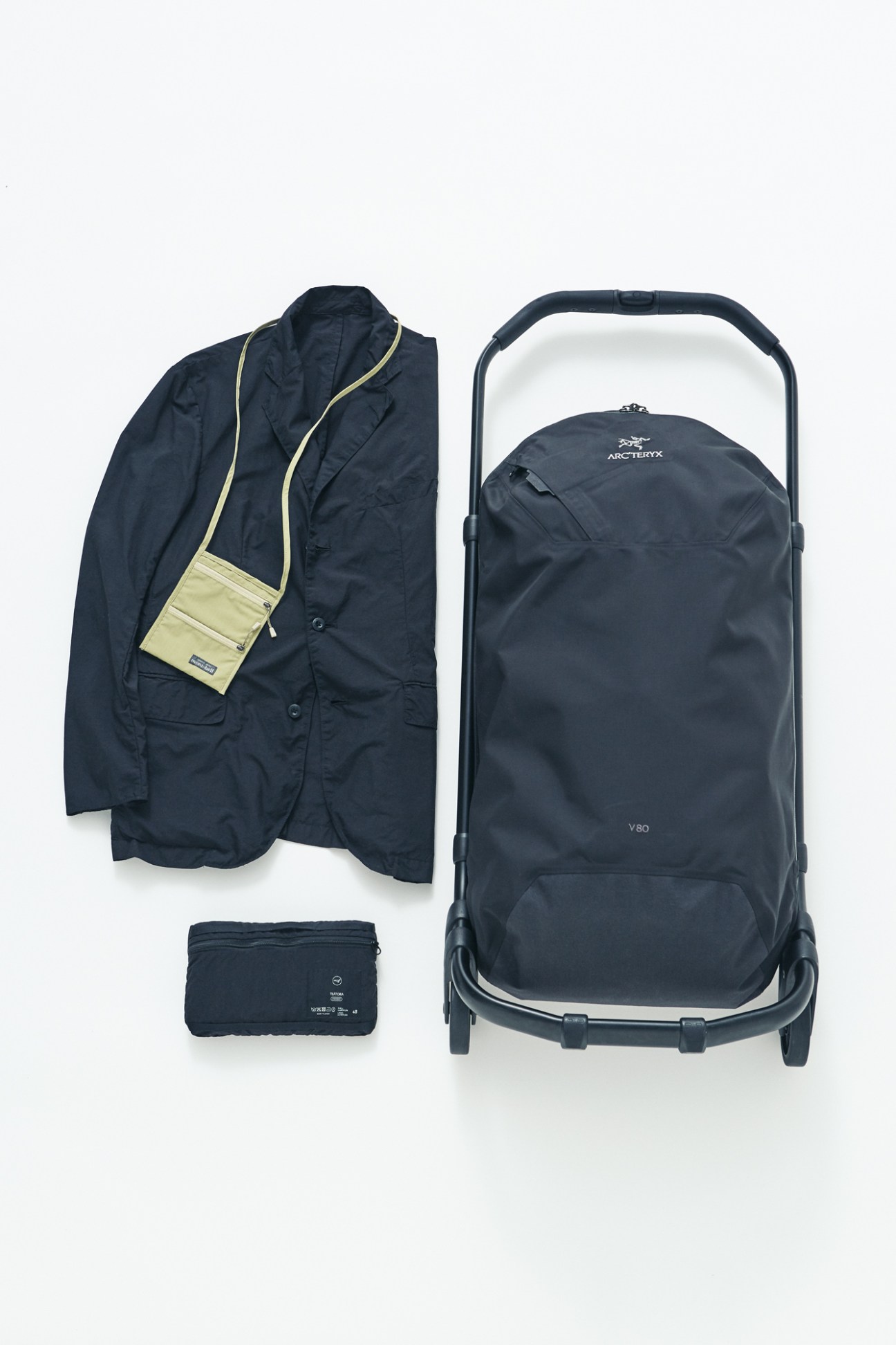 Navy Arc'teryx suitcase with jacket, shoulder bag, and small pouch arranged on white background.