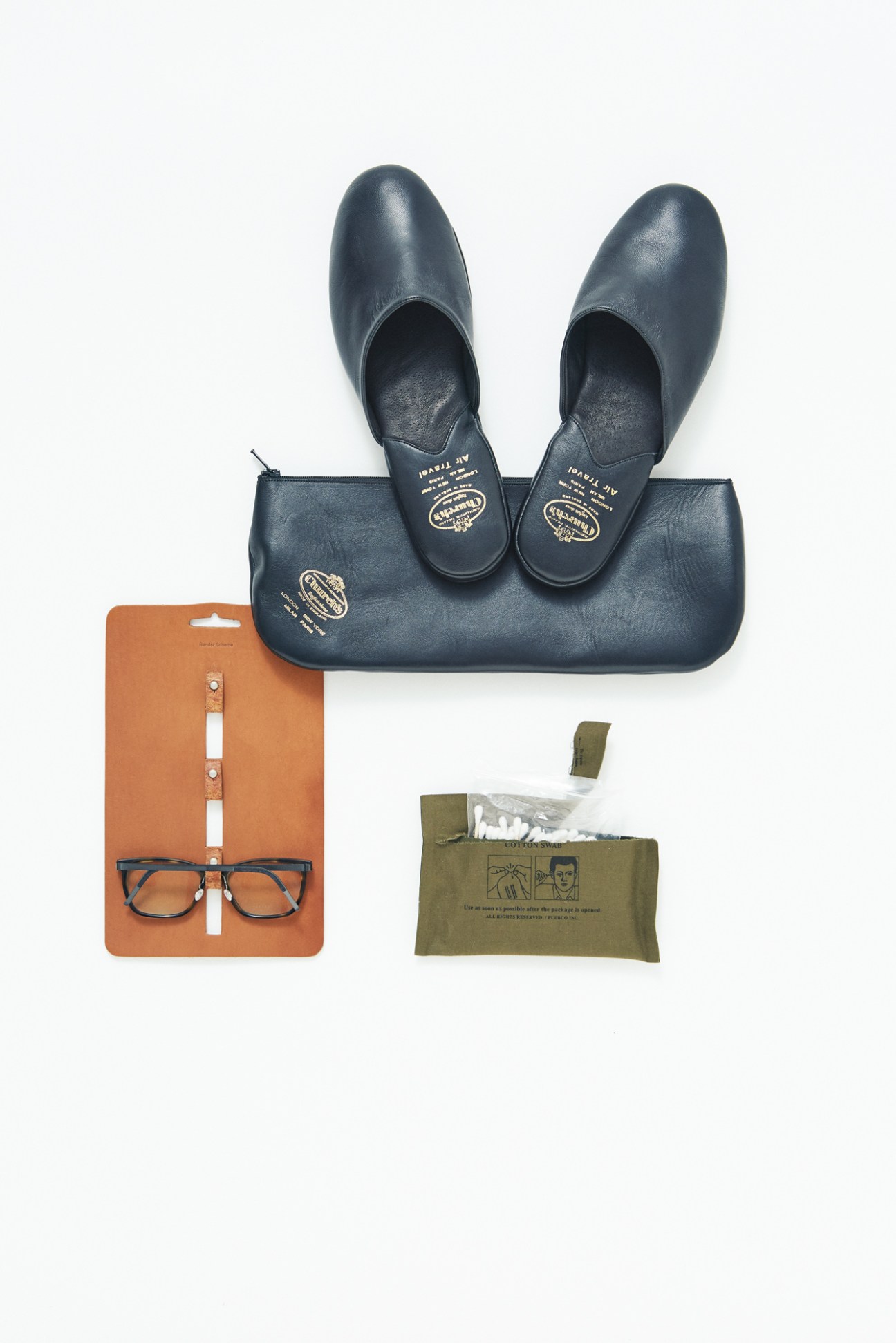 Navy leather slippers by Church's with an orange leather glasses holder by Hender Scheme, dark-framed glasses by Lindberg, and a green pouch of cotton buds by Puebco.