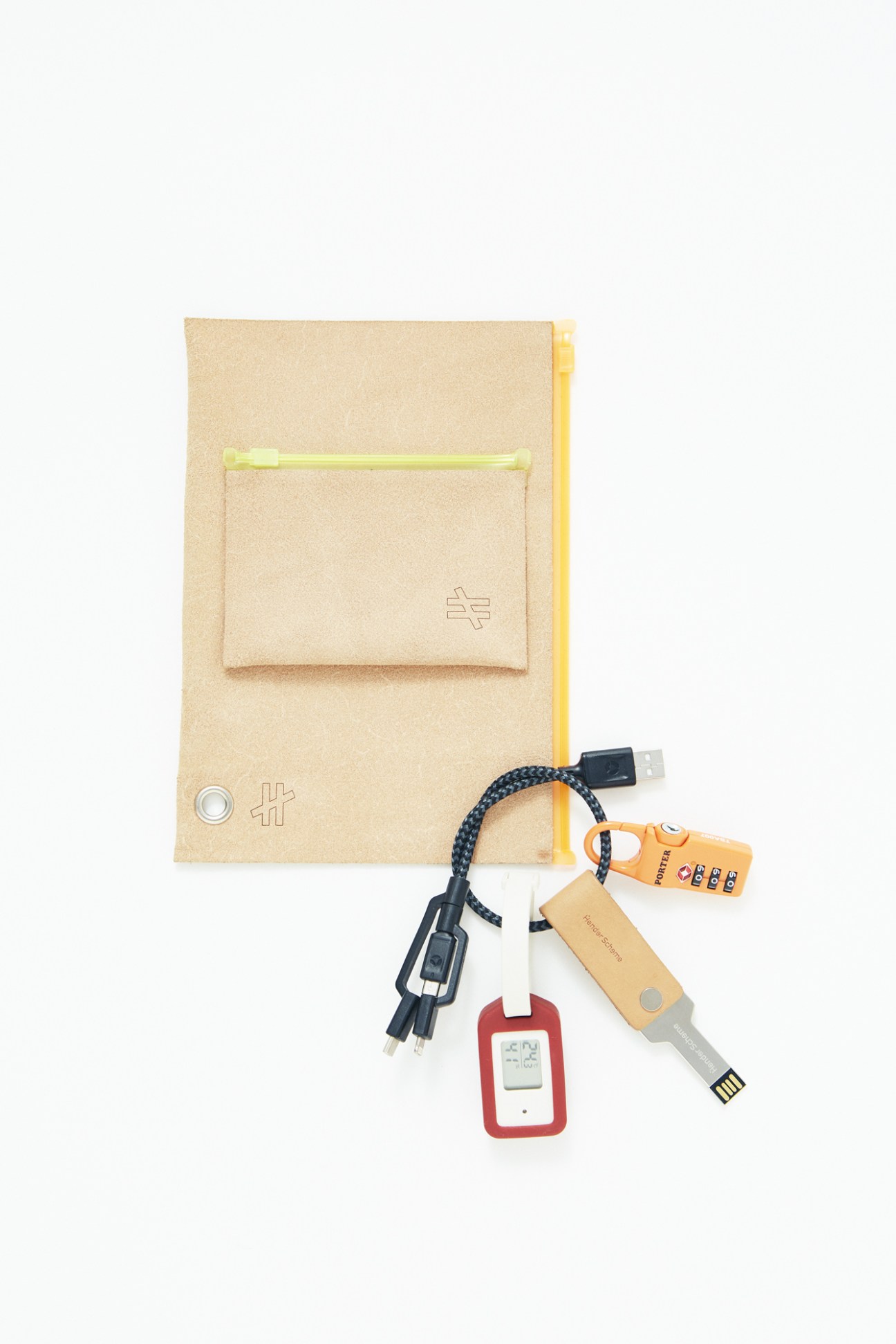 Travel accessories including Kiruna pouches, Nomad USB cable, Porter suitcase key, Hender Scheme USB stick, and Muji thermometer tag arranged on white background.