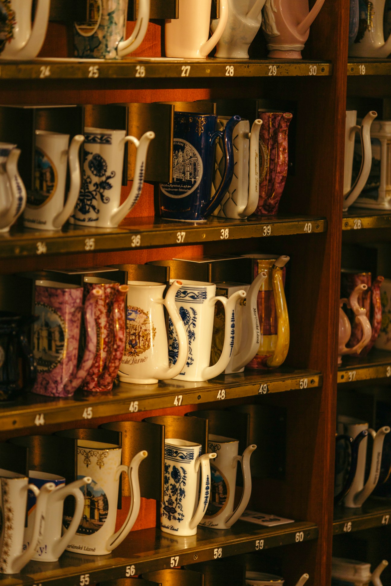 Shelves displaying numbered ceramic spa cups with decorative handles in various patterns and colors