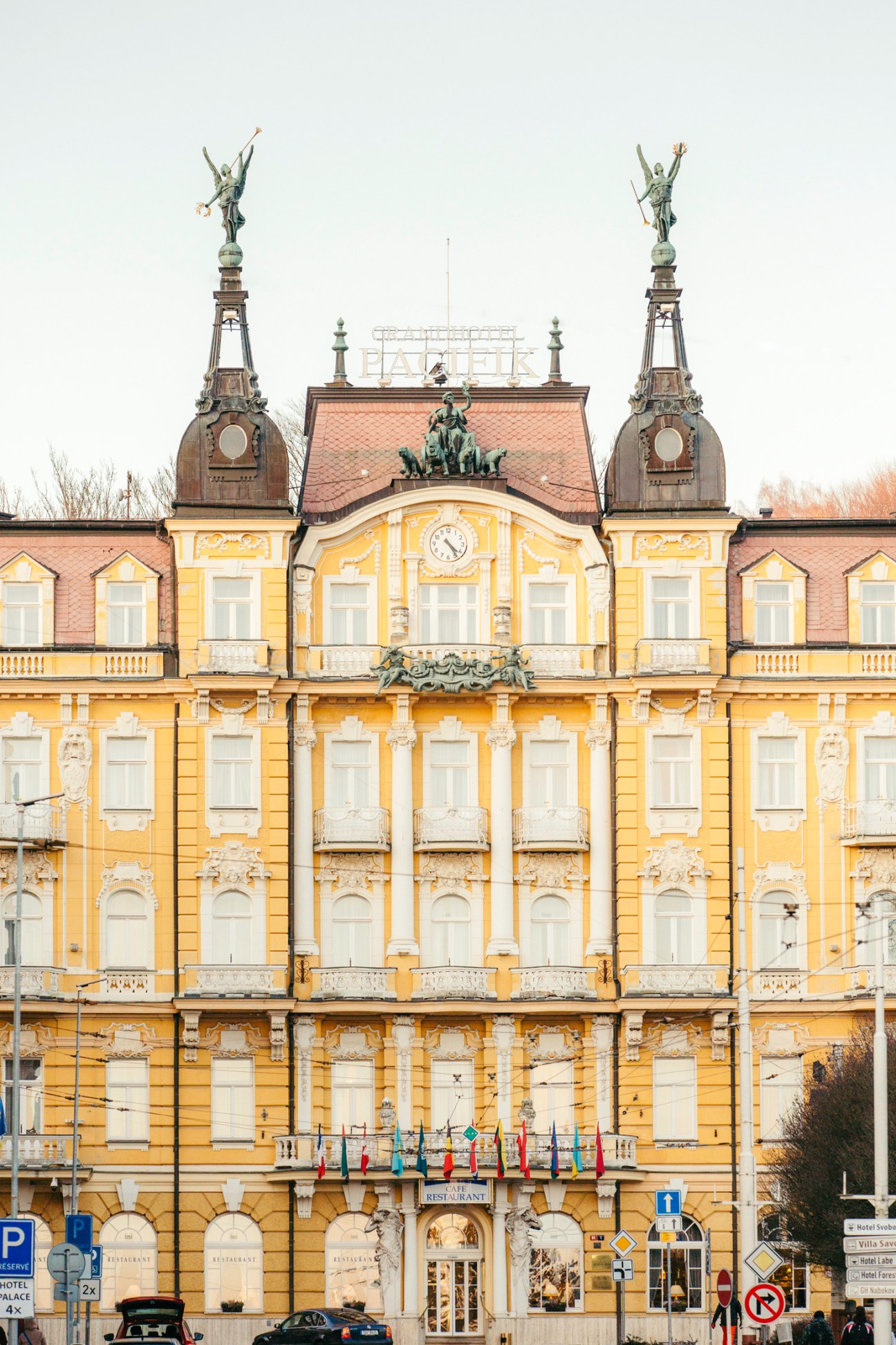 Yellow neo-baroque hotel building with ornate white details, twin spires topped with winged statues, and a central clock