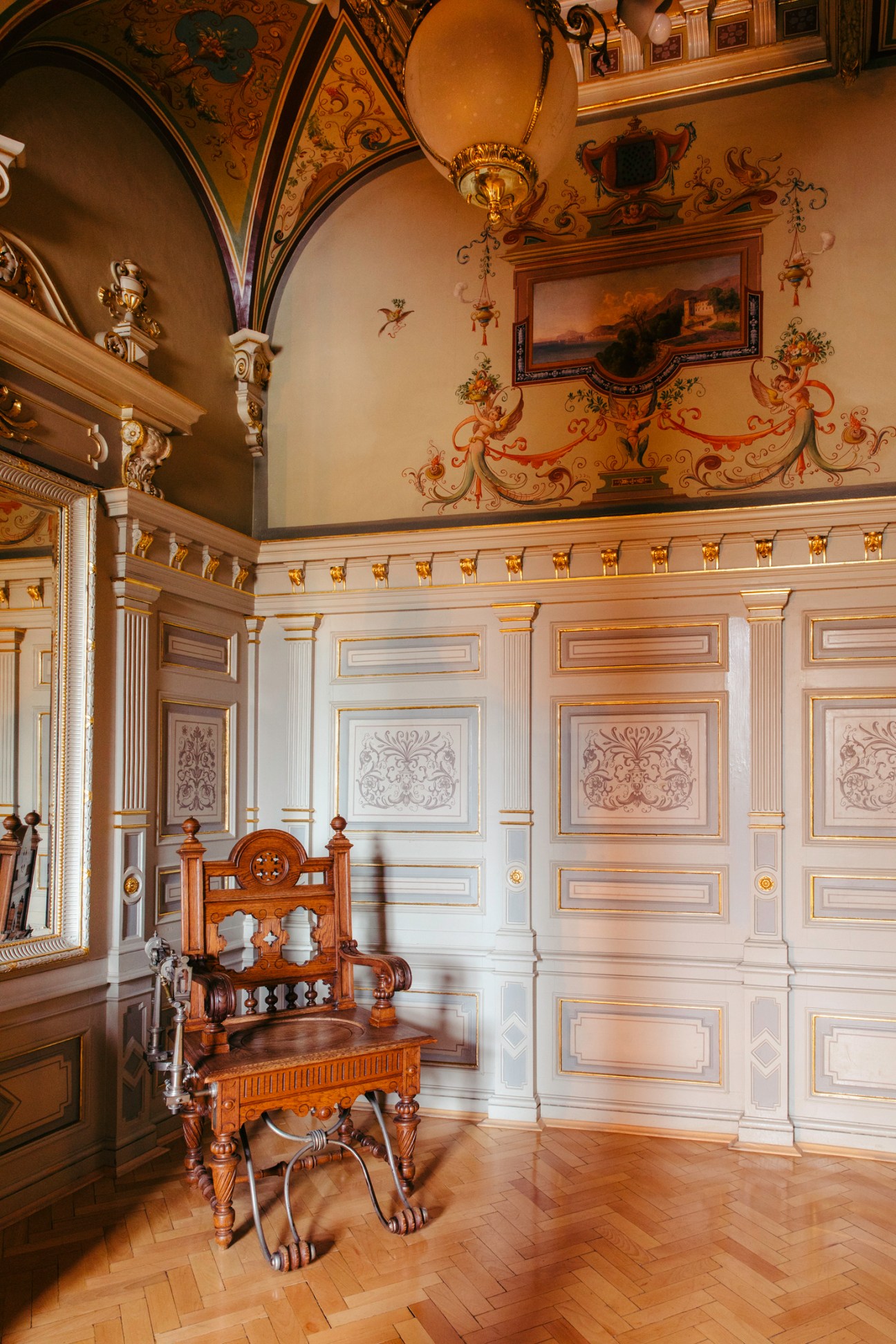 Ornate interior with decorative ceiling, painted walls, white paneled wainscoting, and carved wooden chair