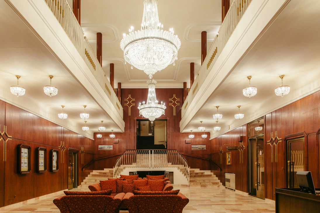 Grand hotel lobby with crystal chandeliers, marble floors, red seating and ornate wooden paneling
