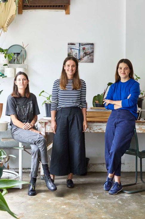 Three women standing in a bright shop interior with plants and shelving.
