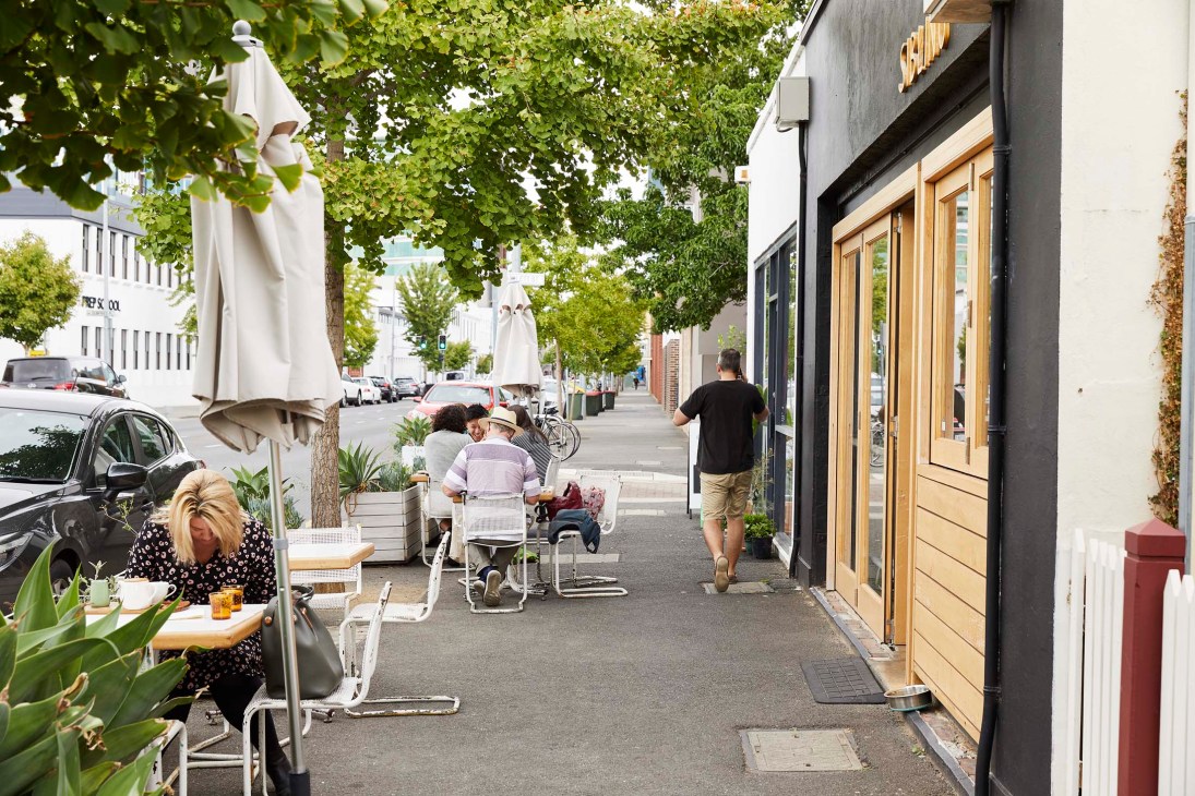 A tree-lined street with outdoor seating, green awnings, and pedestrians walking past storefronts in Adelaide.