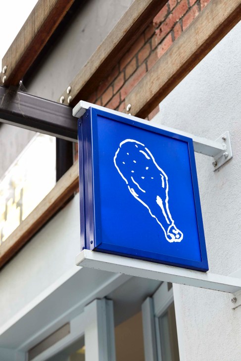 Blue restaurant signage with white outline illustration of a chicken leg hanging from wooden beams.