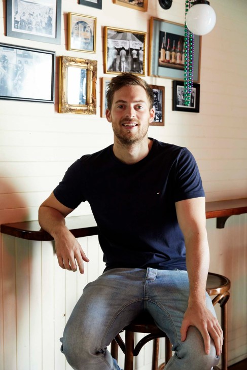 Oliver Brown, director of hospitality group The Big Easy, sitting on a stool in front of a gallery wall.