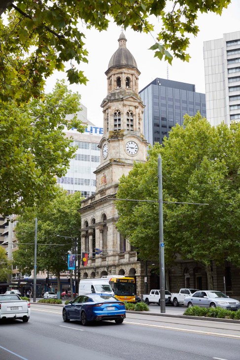 Adelaide Town Hall, a heritage stone building with a domed clock tower, surrounded by modern buildings and green trees.