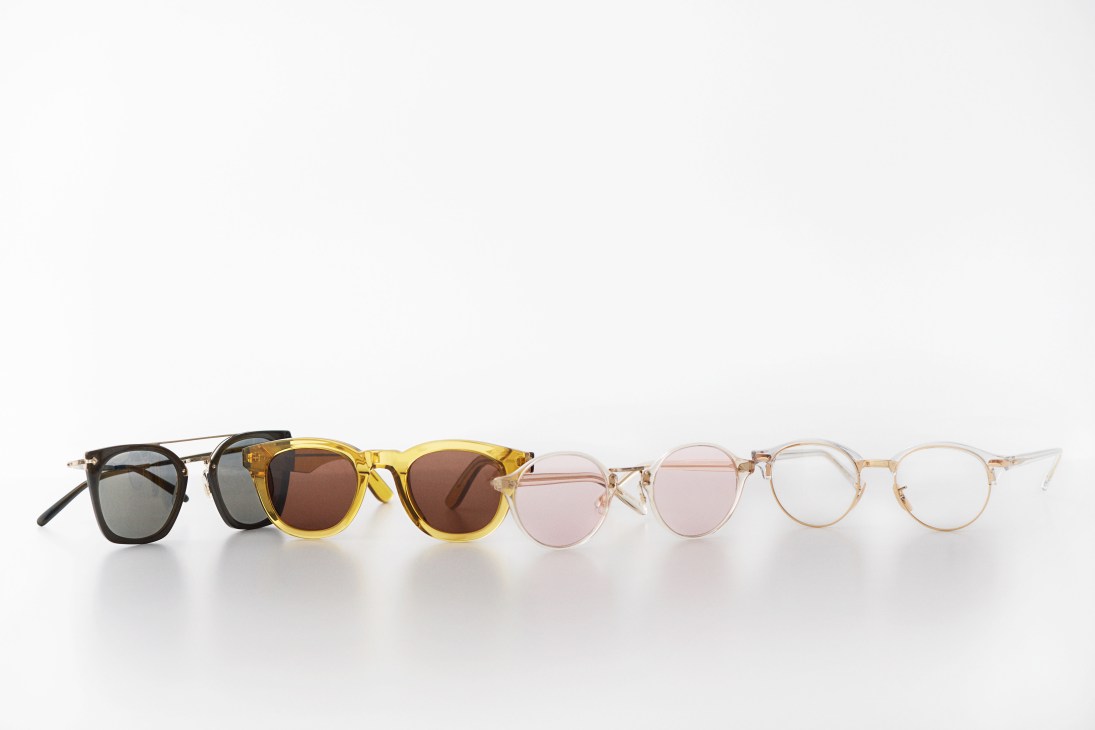 Seven eyeglasses in various styles and colors arranged in a line against a white background.