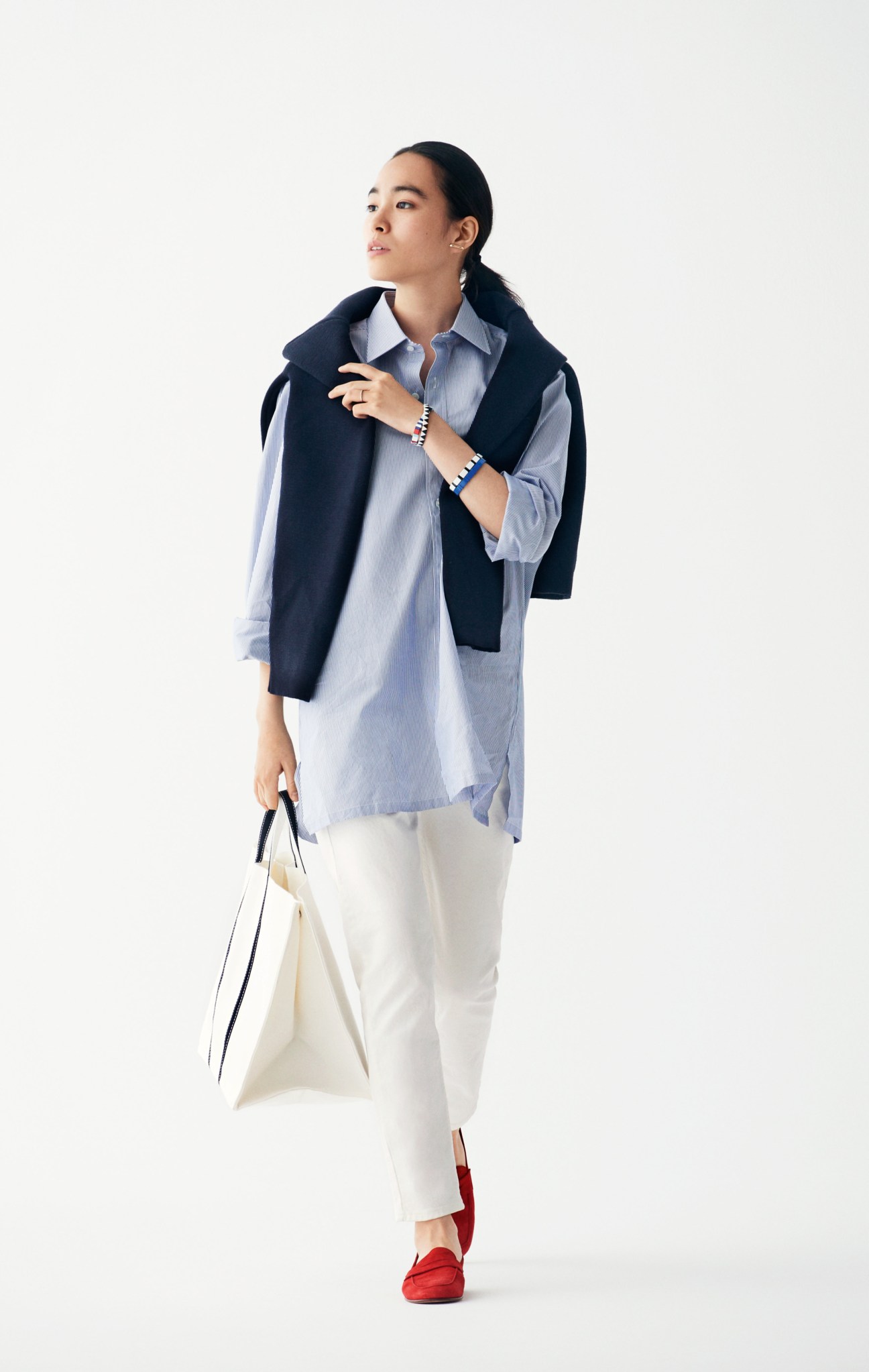 Woman wearing Connolly jumper and Charvet shirt with white jeans and red Mansur Gavriel shoes, holding a cream Tembea bag.
