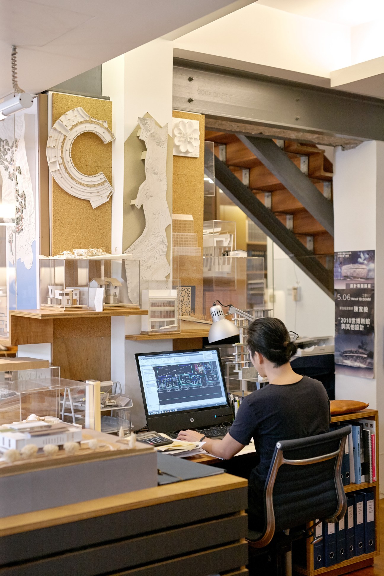 Architect working at desk with laptop surrounded by architectural models and design materials in studio.
