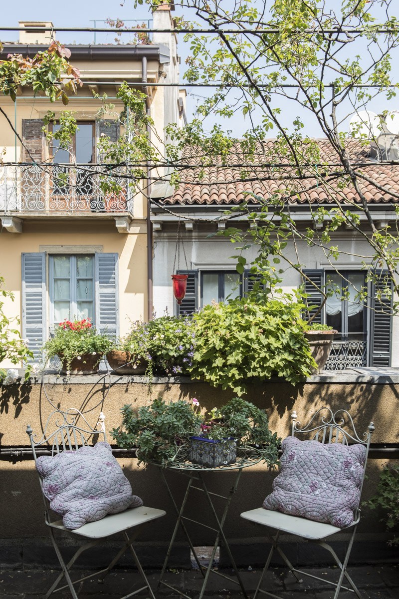 A rooftop terrace in Milan's Brera neighbourhood with climbing vines, potted plants, and two chairs overlooking historic buildings.