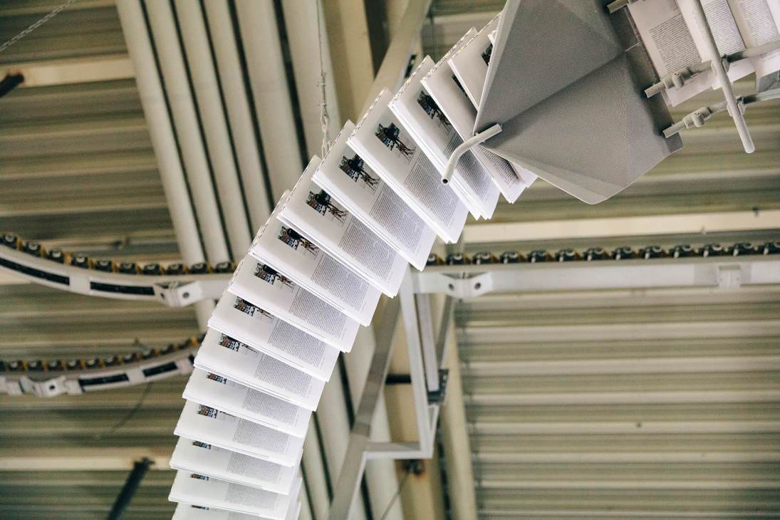 Magazine sections hanging and clipped together in sequence for binding at a printing facility.