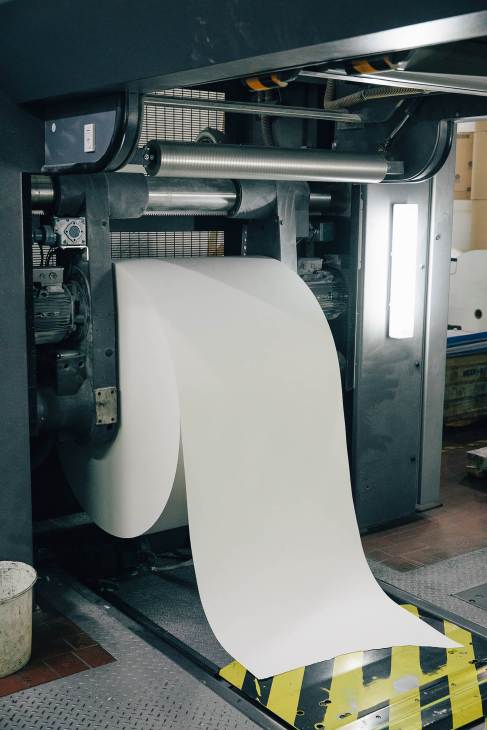 Large roll of white paper being fed through printing press machinery.