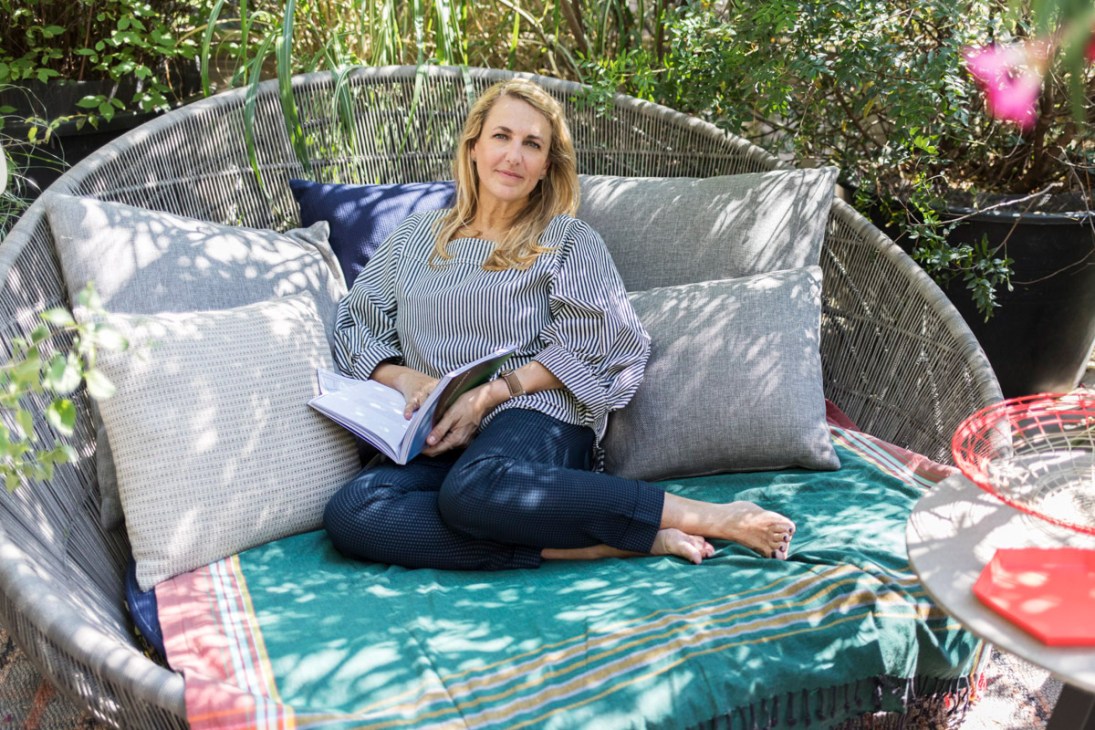 Designer Patricia Urquiola sits on a woven chair surrounded by lush greenery on her Milan rooftop terrace.