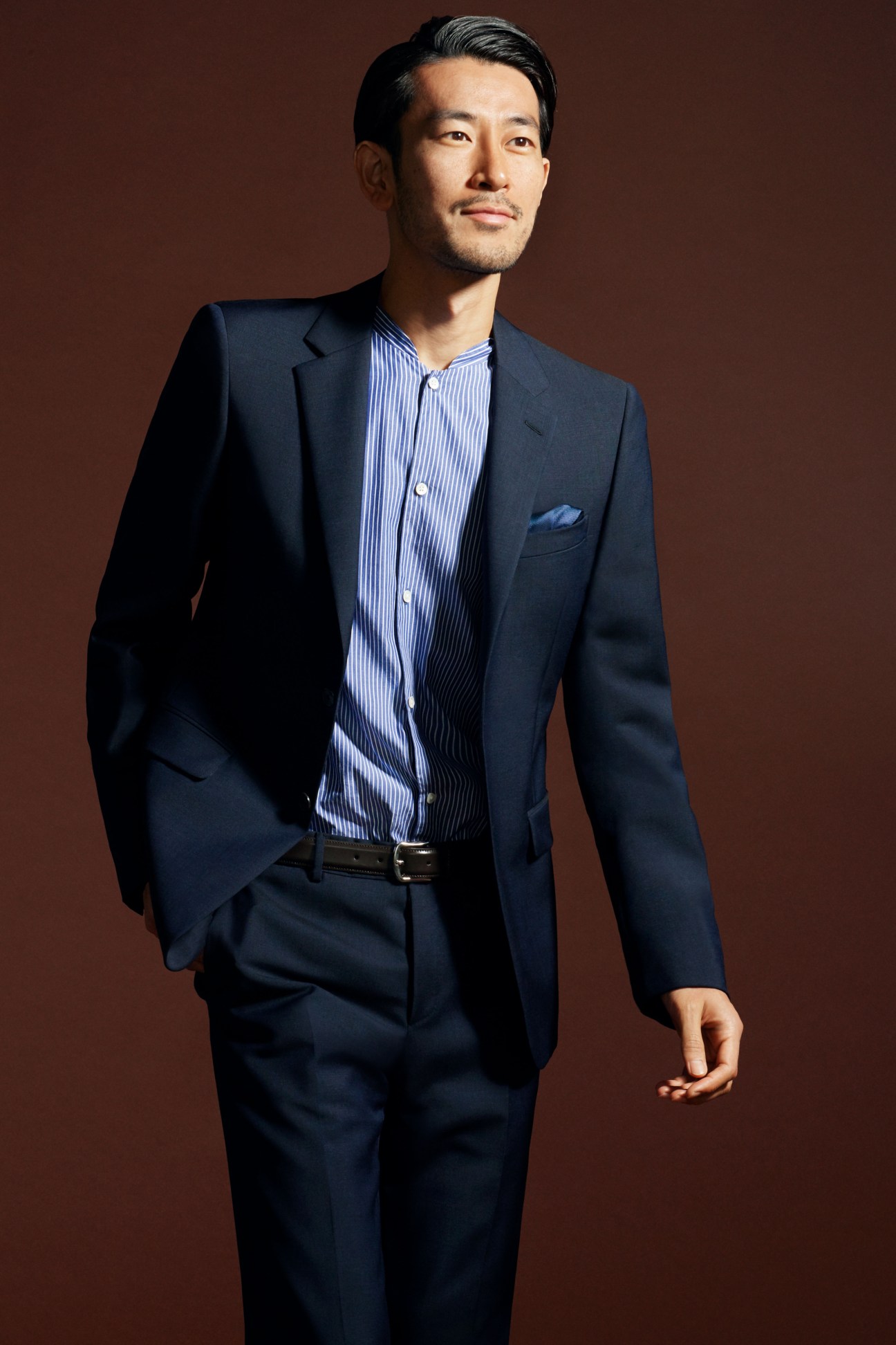 Man in dark navy Prada suit with striped shirt and pocket square against brown background