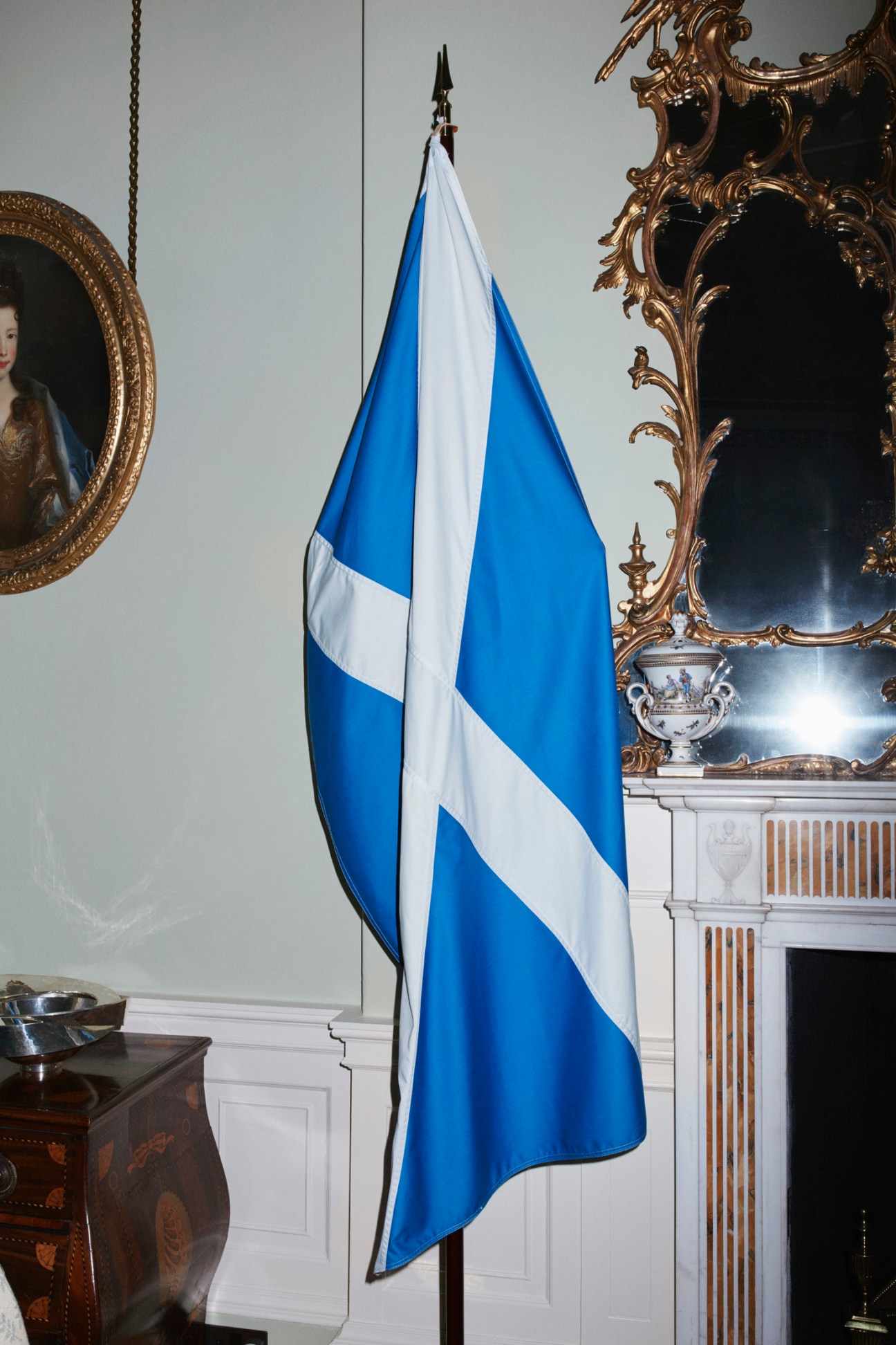 Scottish saltire flag displayed next to an ornate gilded mirror and fireplace mantel in Bute House.